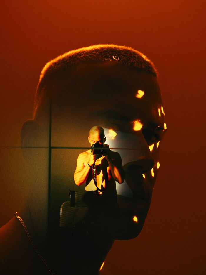 Oliver Takáč captures a shirtless man taking a photo, with reflections of neon lights creating a cinematic portrait.