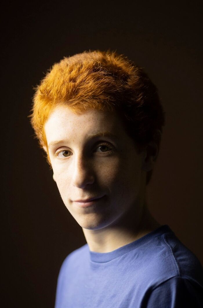 Young natural redhead boy with short curly hair and freckles, smiling for the global portrait project.