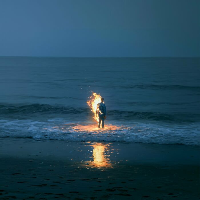 A Luca Ponsato surreal work: a figure on fire stands in the ocean as waves crash, exploring human emotions.
