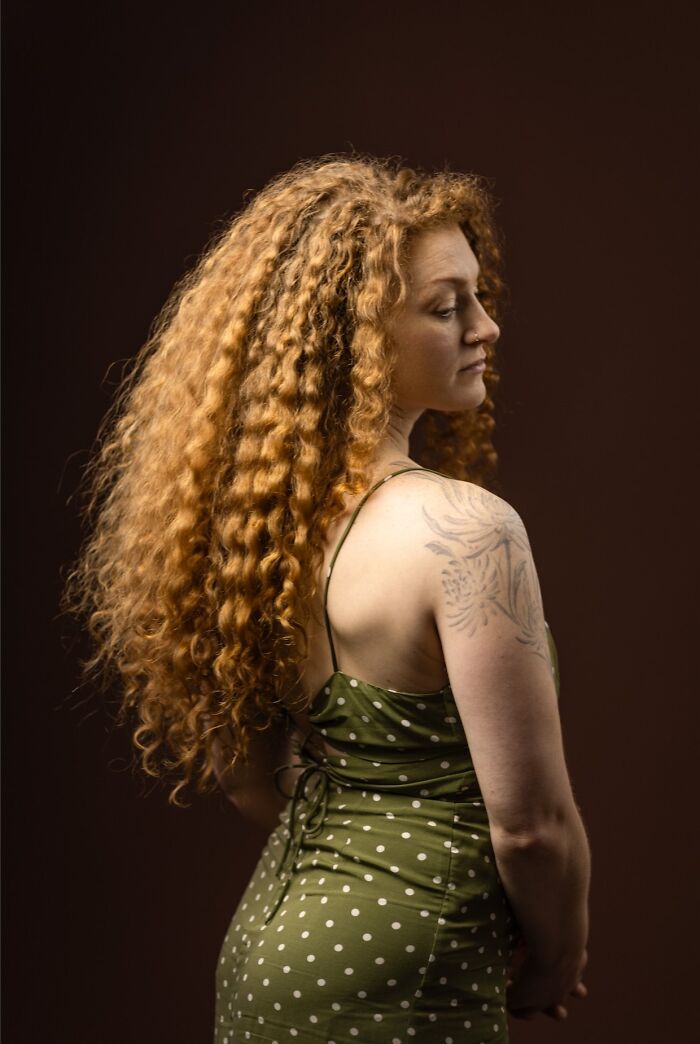 Back view of a woman with long, curly natural red hair, showcasing her beauty in the portrait project.