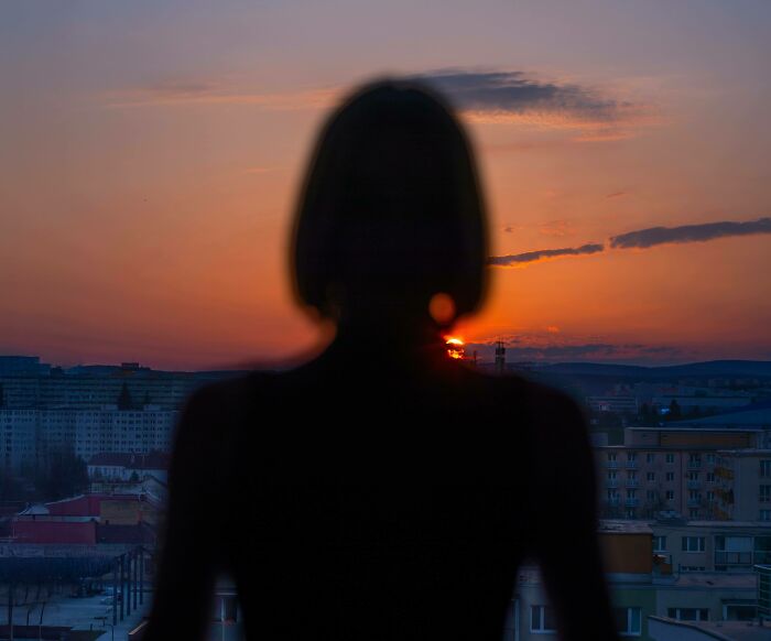 A silhouette of a woman looking at a sunset over a city, creating a cinematic portrait.