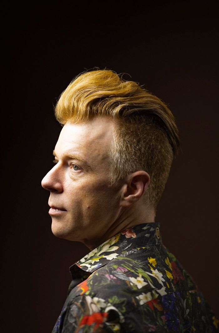 A man with natural redheads hair styled in an undercut, wearing a floral shirt, looking to the side.