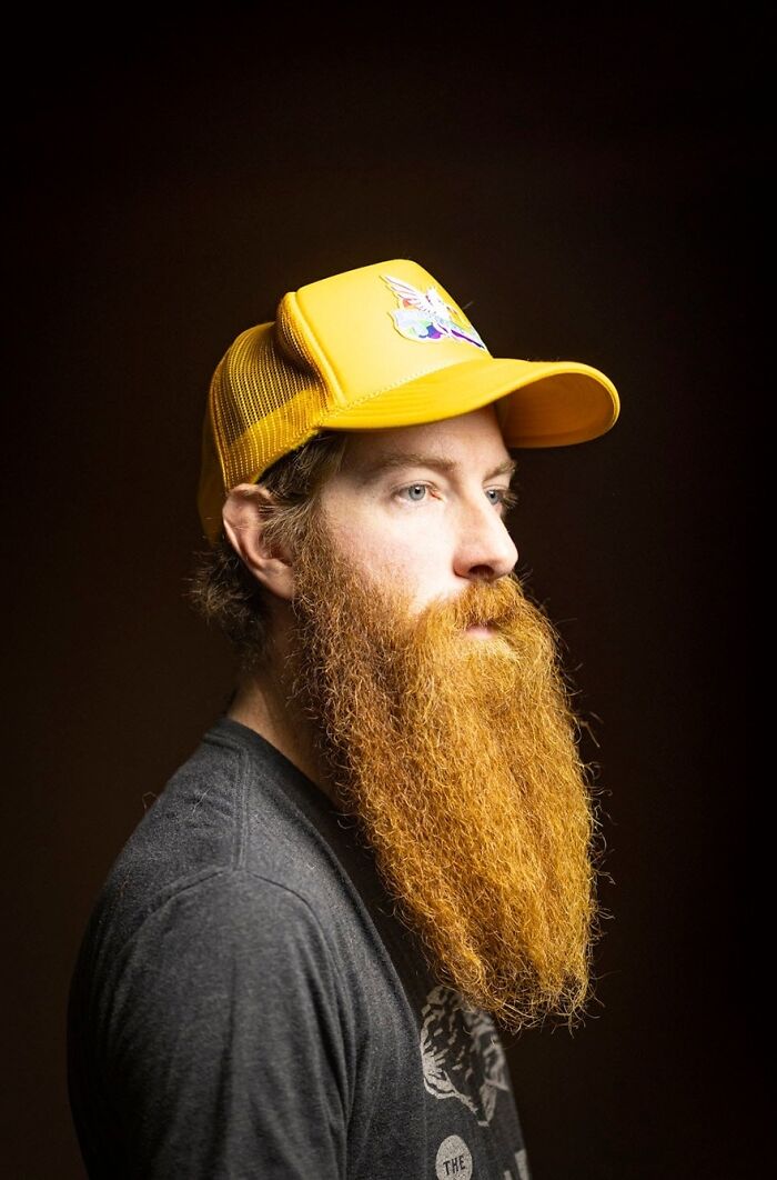 A man with a long, thick natural redheads beard and a yellow cap, looking to the side.