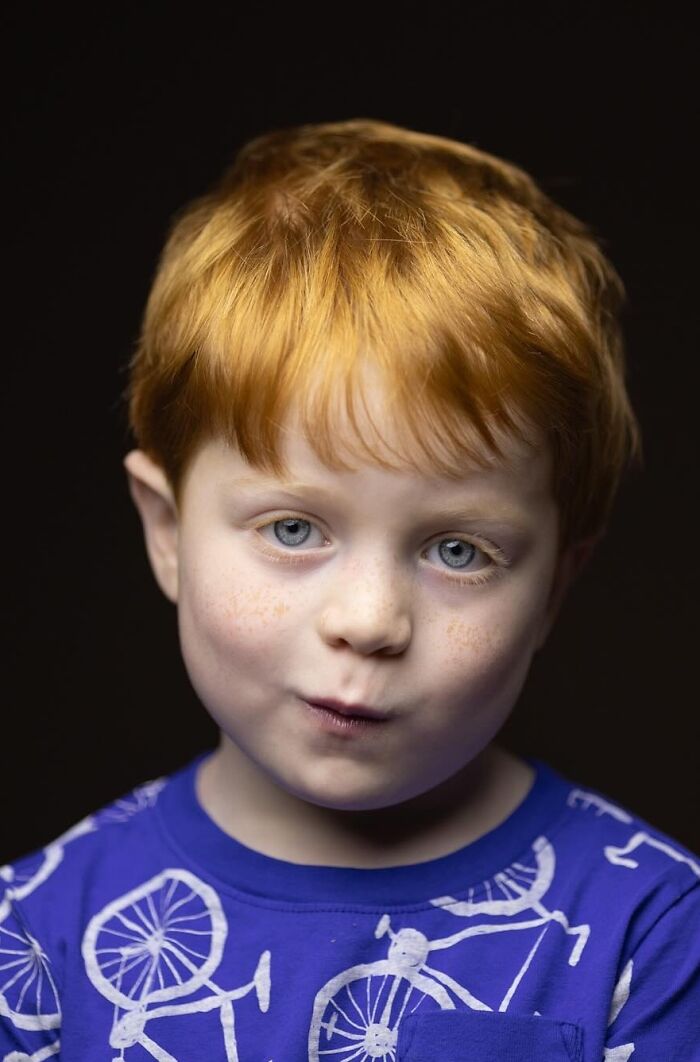 A young boy with natural redheads, blue eyes, and freckles, wearing a blue shirt.