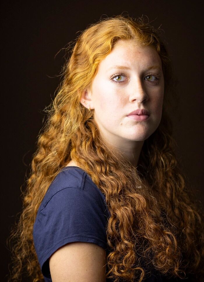A striking portrait of a young woman with long, curly natural red hair, showcasing her vibrant locks.