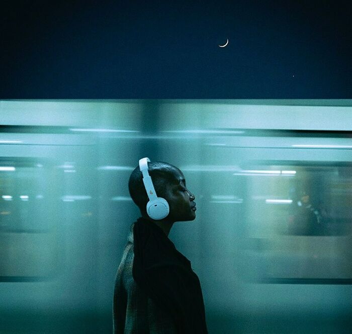 Oliver Takáč cinematic portrait of a person with headphones, looking up at a crescent moon in a night sky.
