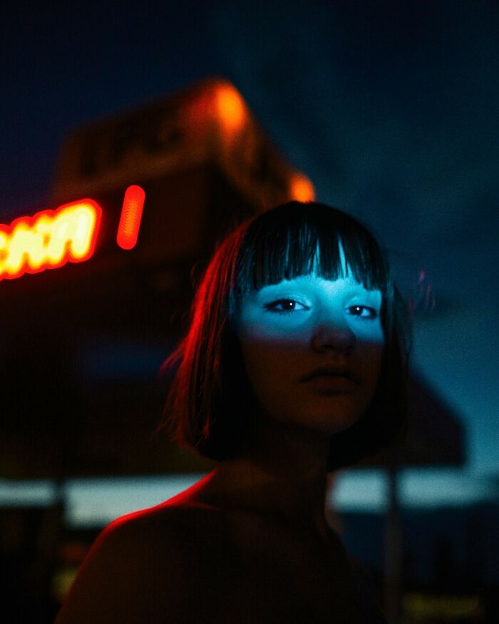 Oliver Takáč cinematic portrait of a woman with bangs, blue light on her face, neon lights in the background.