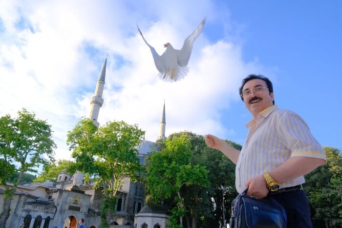 A candid moment from the streets: a man smiling as a white bird flies overhead near a mosque.