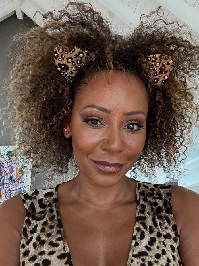 Mel B, a famous celebrity, smiling while wearing leopard print and cat ears, discussing dating experiences.