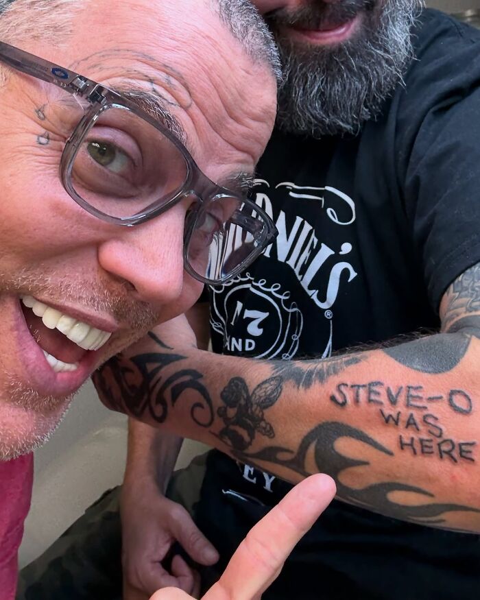 Steve-O pointing to a tattoo on a man's arm that reads 'Steve-O Was Here,' humorously depicting celebrity dating.