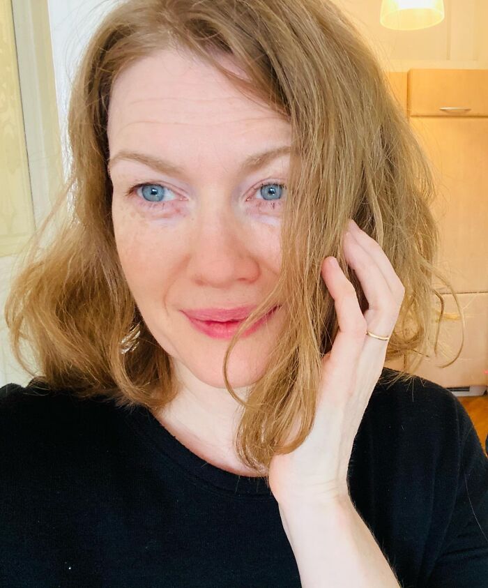 A woman with red hair and blue eyes poses for a photo, her hand touching her cheek, offering a glimpse into dating a celebrity.