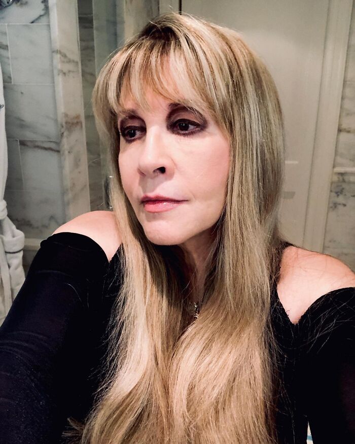 Stevie Nicks, a celebrity, with long blonde hair and dark eye makeup, looking to the side.