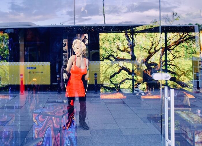 A candid moment from the streets: a woman in a bright orange dress reflects in a glass window.