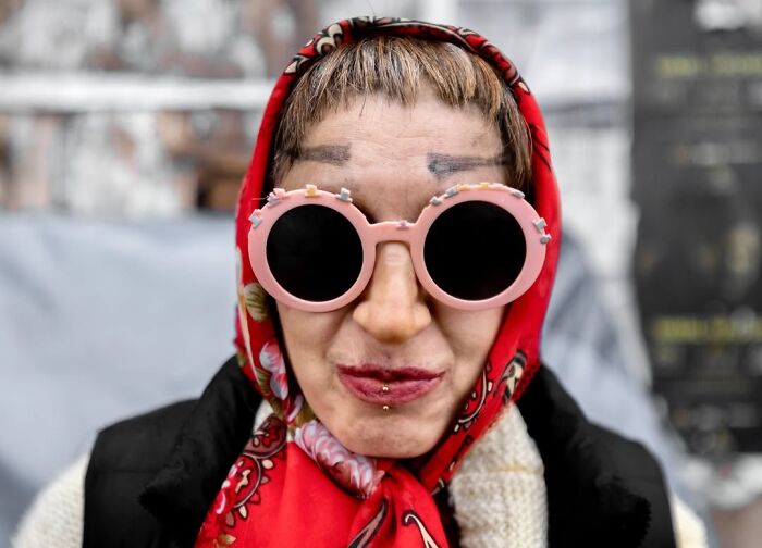 A candid moment from the streets: a person in a red headscarf and pink round sunglasses, by Sami Uçan.