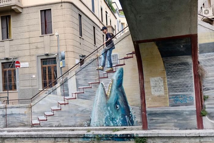 A candid moment from the streets by Sami Uçan shows a person walking down stairs with a shark mural.