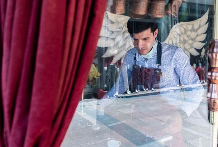 A candid moment from the streets by Sami Uçan shows a man with angel wings behind him, reflected in a window.