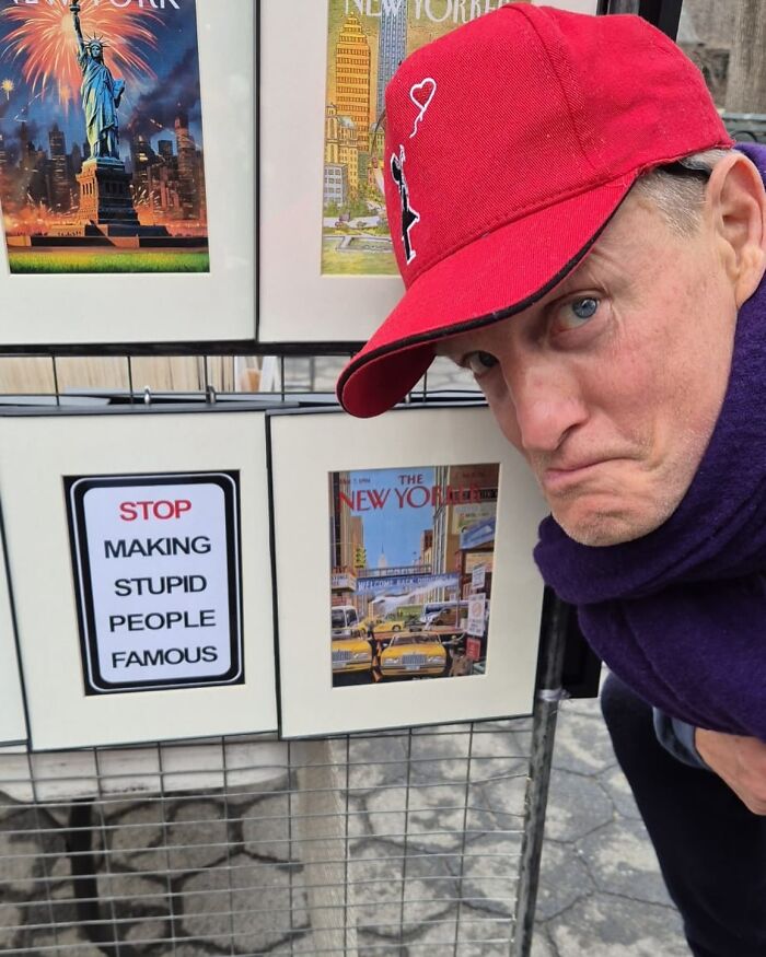 Man making a face next to a sign saying STOP MAKING STUPID PEOPLE FAMOUS, reflecting on celebrity culture.
