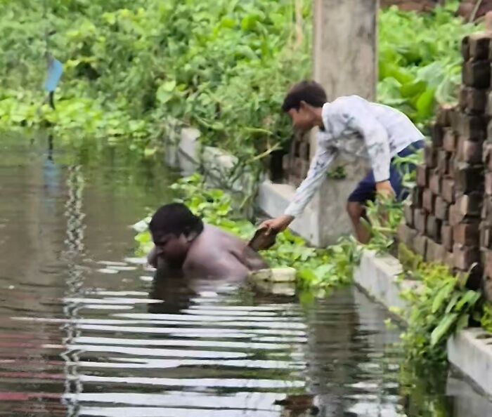 Teen with mysterious condition in a pond, receiving help from another person on the bank.