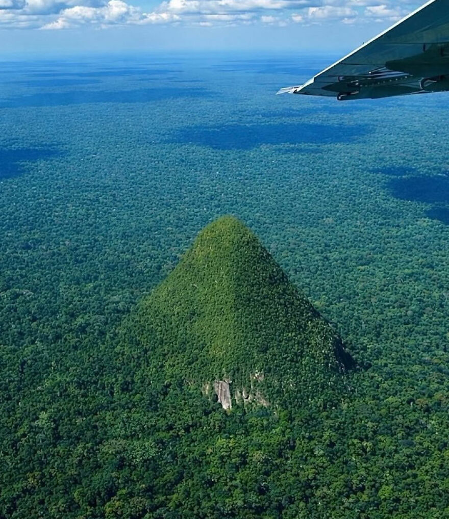 Aerial view of a strange, perfectly cone-shaped mountain covered in dense forest, a wonder of Earth.