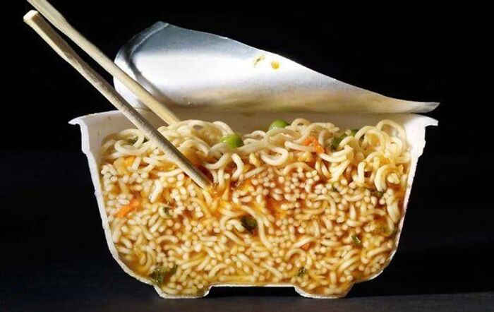 Photo of an object cut in half, showing a cross-section of instant noodles in a cup with chopsticks.
