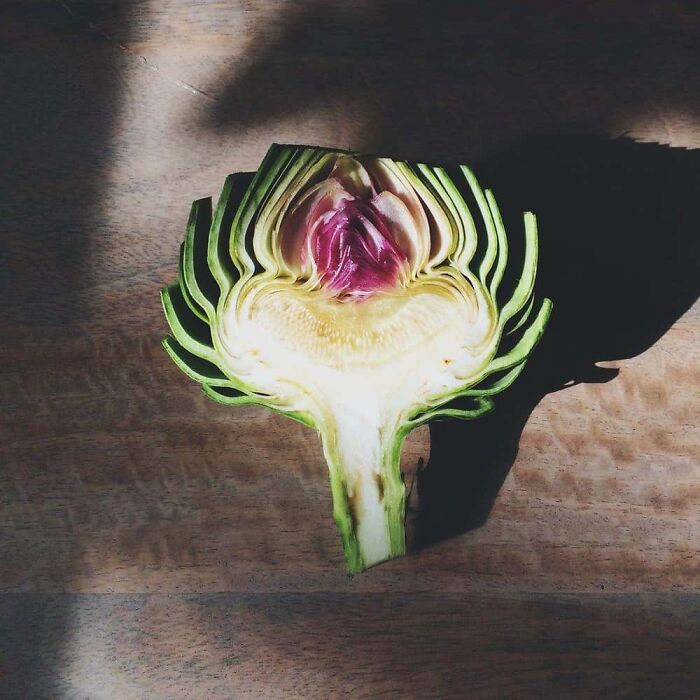 Interesting photo of an object cut in half: an artichoke showing its vibrant purple and green layers.