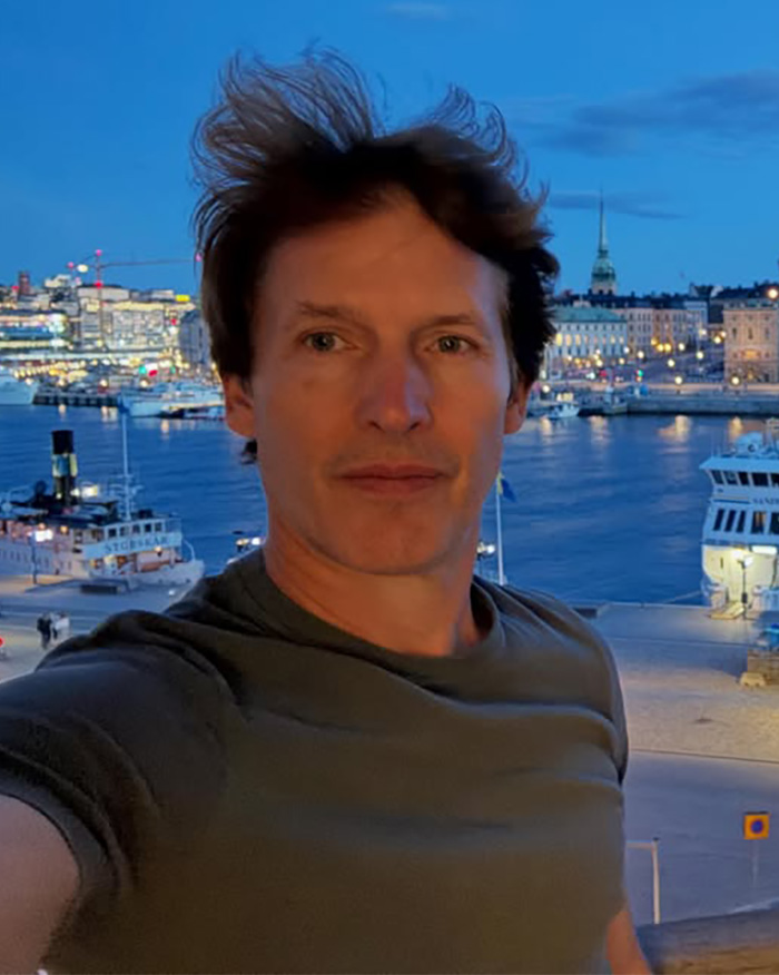 Singer James Blunt in a selfie photo outdoors with a city skyline and boats in the background. Singer James Blunt in a selfie photo outdoors with a city skyline and boats in the background.