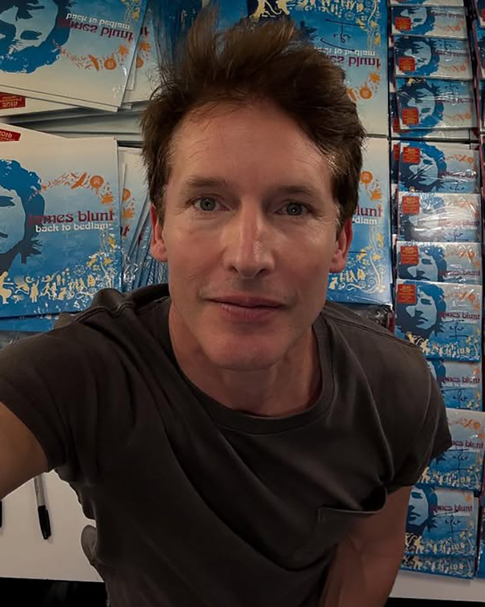 Singer James Blunt in a dark grey t-shirt, standing in front of shelves filled with copies of his album Back to Bedlam. He is looking directly at the camera. Singer James Blunt in a dark grey t-shirt, standing in front of shelves filled with copies of his album Back to Bedlam. He is looking directly at the camera.