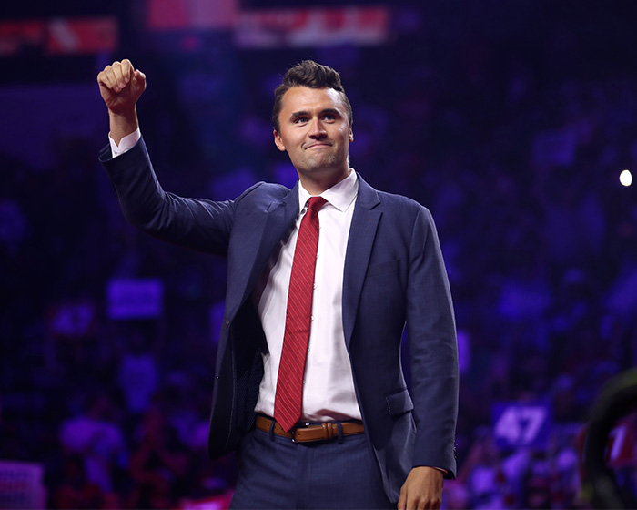 JD Vance on stage, raising a fist, wearing a navy suit and red tie. JD Vance on stage, raising a fist, wearing a navy suit and red tie.