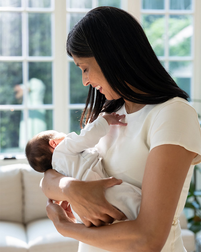 Usha Vance smiles while cradling her newborn son, gentle light from a window illuminates them. Usha Vance smiles while cradling her newborn son, gentle light from a window illuminates them.