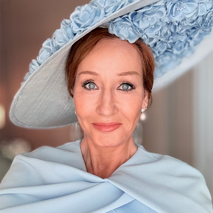 J.K. Rowling in an elegant blue dress and a large, wide-brimmed hat adorned with blue flowers.