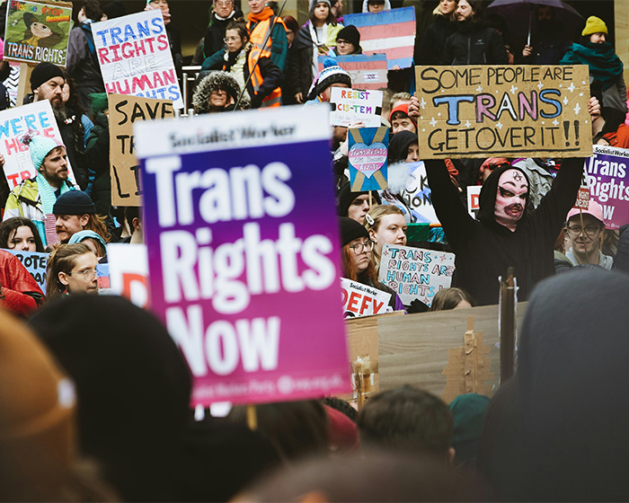 A crowd of people at a rally holding signs related to trans rights and transgender surgery.