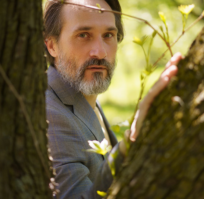 A man with a beard peaking from behind a tree, illustrating one of the weird jobs people do.