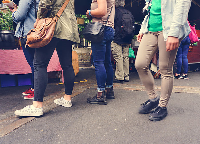 People's legs and feet are visible on a paved surface, moving past market stalls, suggesting weird jobs at a street market.