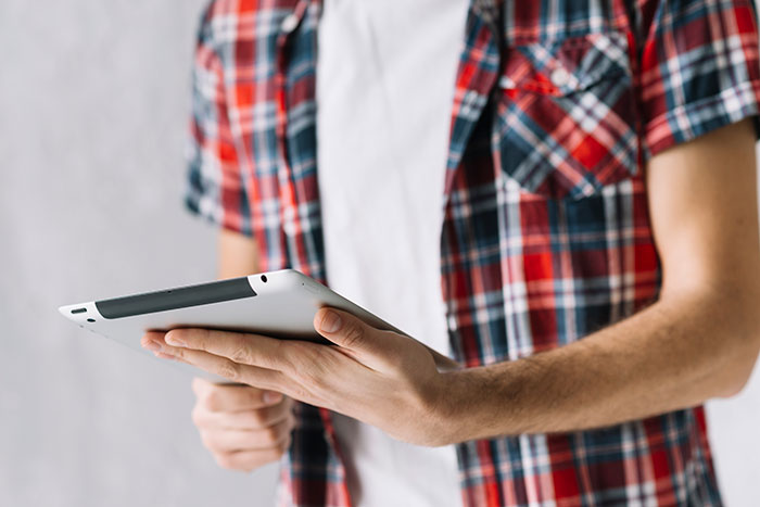 A person in a red and blue plaid shirt holds a tablet, perhaps researching weird jobs or performing one digitally.