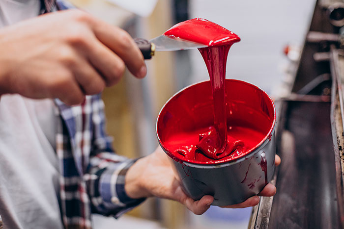 A person holding a can of thick red paint with a spatula, highlighting a hands-on job, potentially weird.