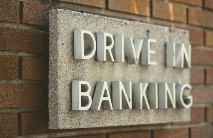 A Drive-In Banking sign on a brick wall, reflecting customers interactions at a drive-through.