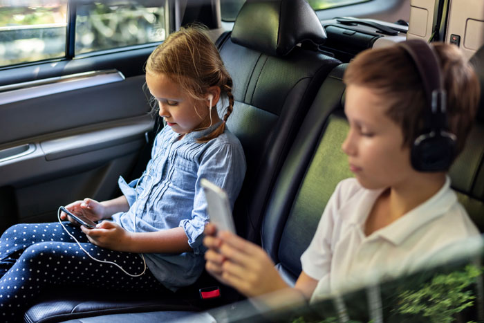 Two children in a car using phones, oblivious to the shopper's weapon threat.