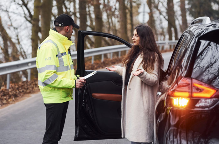 A police officer in a high-visibility jacket talking to a woman next to a black car on the side of a road, related to a shopper accused of having a weapon.