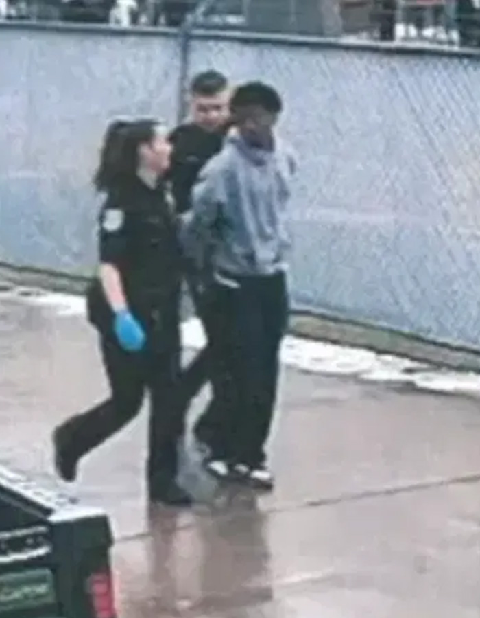 Two police officers escorting a young man in handcuffs, providing evidence for the Karmelo Anthony case. Two police officers escorting a young man in handcuffs, providing evidence for the Karmelo Anthony case.