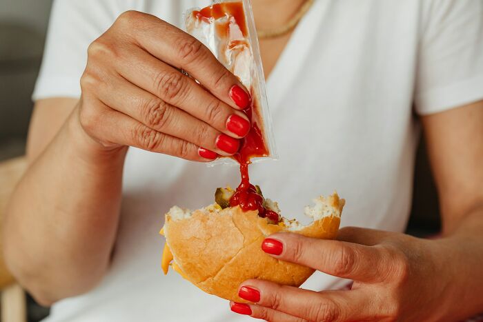 A woman squeezes ketchup from a packet onto a burger, a habit that highlights poverty habits.