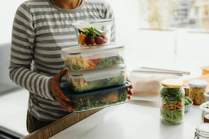 Woman holding stack of meal prep containers, a habit of women to save money.