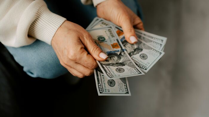 Hands holding several one hundred dollar bills, representing a skill that changed lives in 30 days.