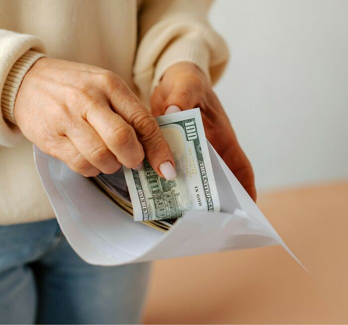 Hands slide a hundred-dollar bill into an envelope, illustrating financial habits beyond poverty.