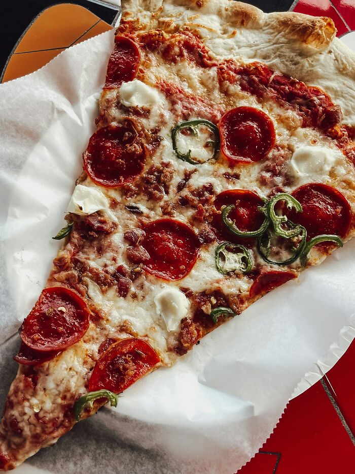 A close-up of a large slice of pizza with pepperoni, sausage, and jalapeños, a delicious surprise in America.