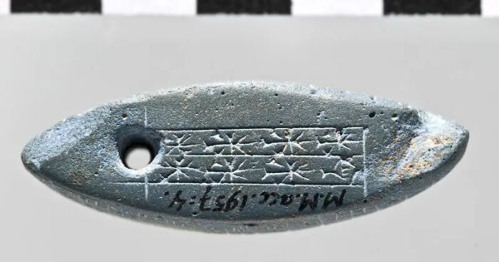 An ancient oval historical artifact, possibly a tablet or stamp, with etched patterns and a hole, reflecting its survival.