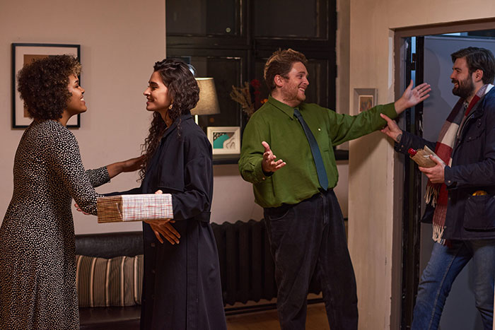 A man arriving at a party with his boyfriend, met by a smiling host, unsure of the welcome.