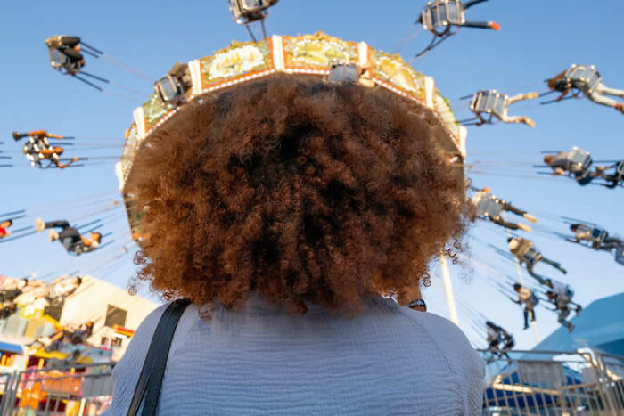 Person with curly hair looking at a spinning carnival ride, a mesmerizing winning photo from the LensCulture Street Photography Awards.