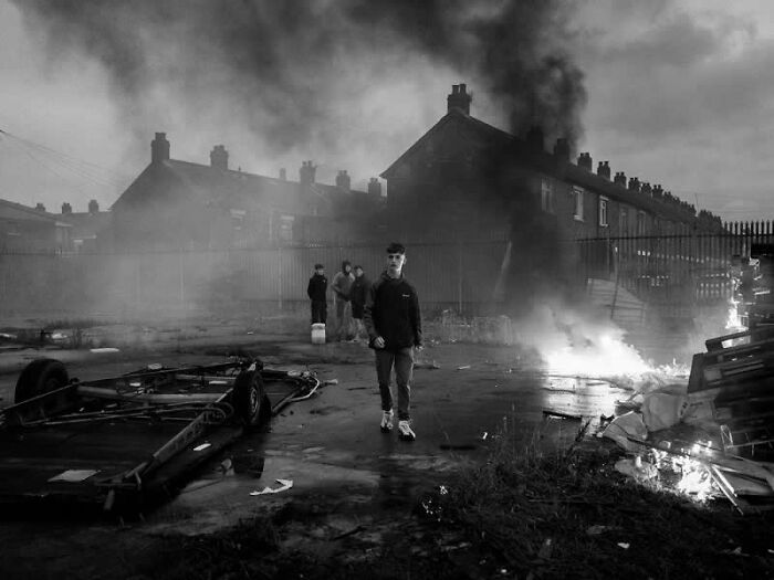 Young man walking through a smoke-filled street with fires, a compelling winning street photography image from the LensCulture Awards.