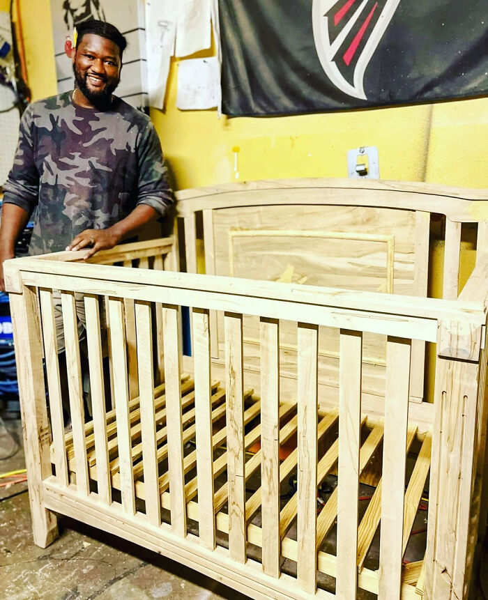 A man proudly stands next to a wooden baby crib, a brilliant DIY home project proving you dont need a huge budget.