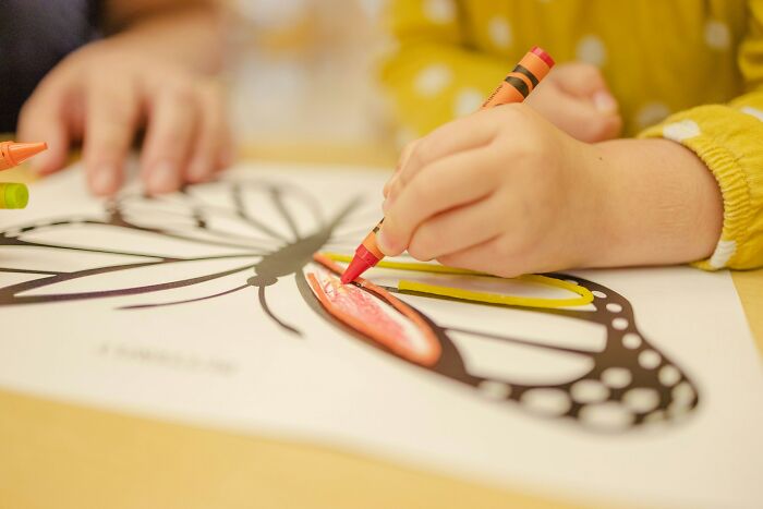 A child colors a butterfly drawing with a crayon, showcasing childhood habits related to poverty.